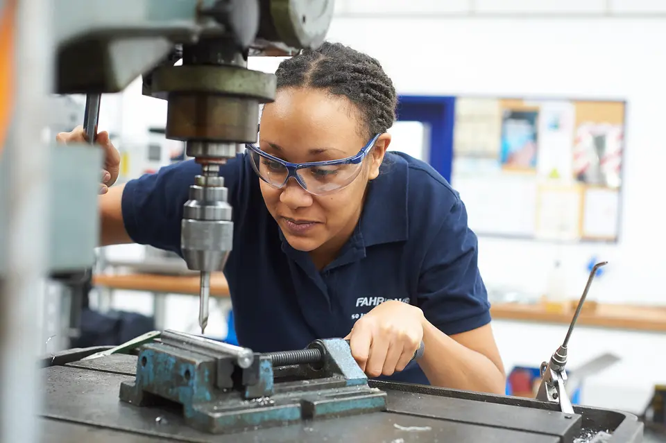 Arbeitswelt bei Fahrion: Mitarbeiterin mit Schutzbrille an der Säulenbohrmaschine in der Werkstatt